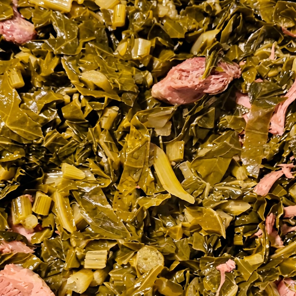 Cooked collard greens with chopped celery and pieces of ham served in a foil tray.