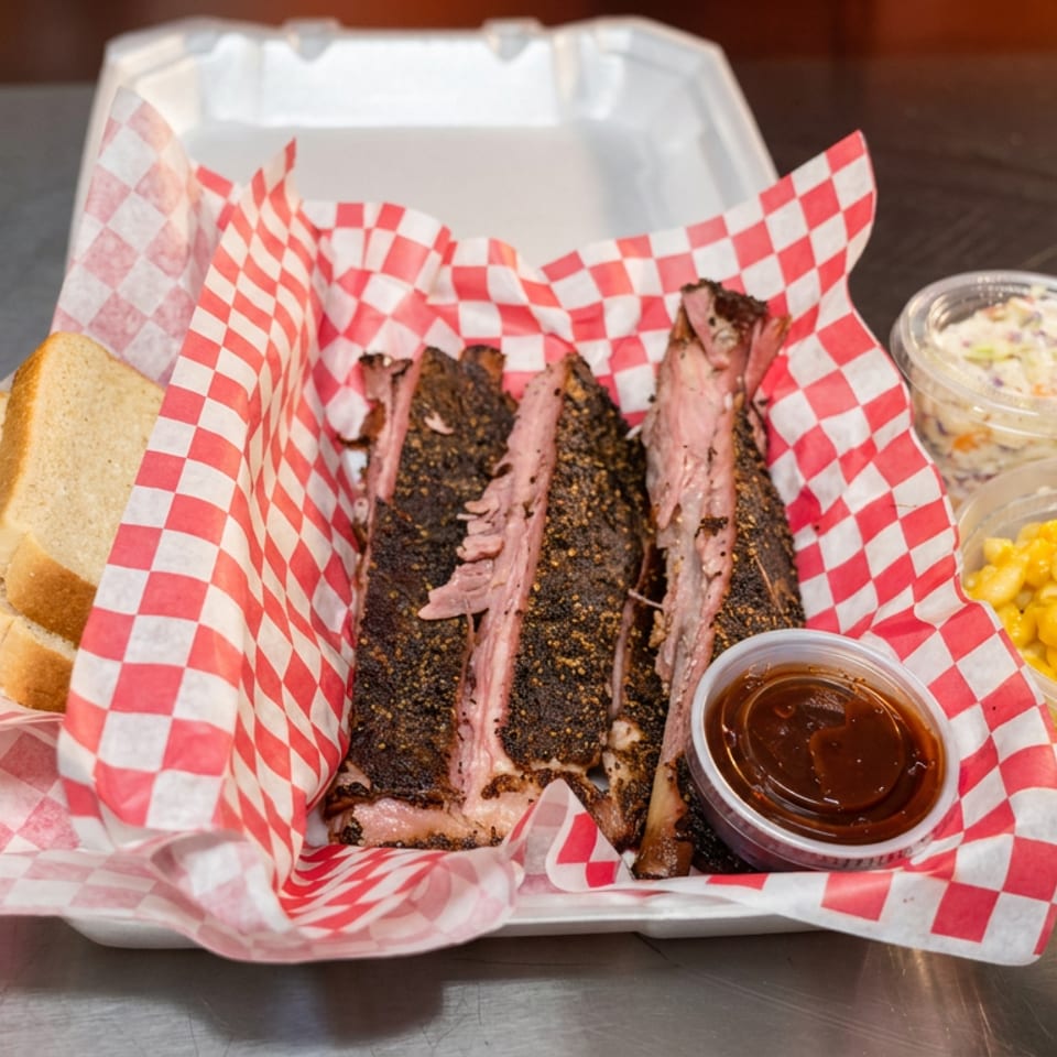 Tray of sliced barbecue brisket with sauce, bread, macaroni and cheese, coleslaw, and a can of Fanta.